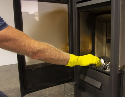 Mies puhdistaa puuhellaa Jøtul F 233 tuhkalla ja vedellä