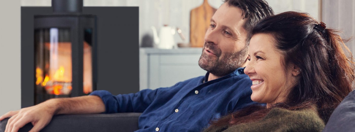 Mies ja nainen istuvat puuhellan edessä Jøtul F 373 Advance olohuoneessa 